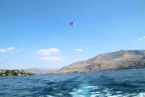 A parasail soaring above a lake, with hills in the background and a clear blue sky.