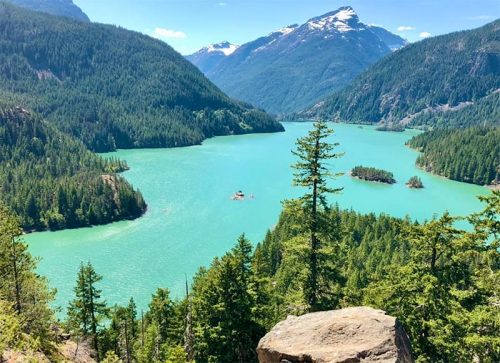 A scenic view of a turquoise lake surrounded by lush green forests and mountains under a clear blue sky.