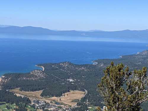 A panoramic view of a lake surrounded by mountains and forests under a clear blue sky.