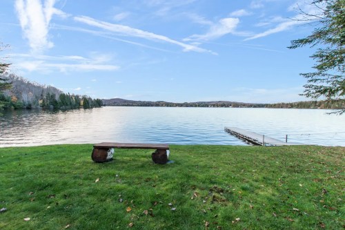 A serene lake view with a grassy shore, a wooden bench, and a dock extending into the calm water under a clear sky.