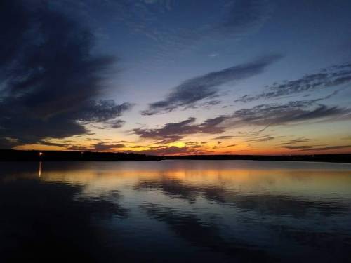 A serene sunset over a calm lake, with vibrant clouds reflecting on the water's surface.