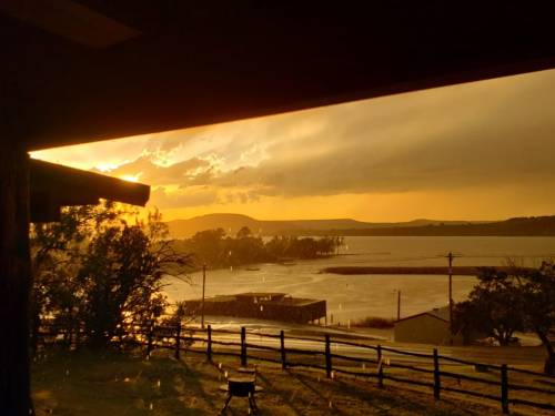 A sunset over a lake, with rain clouds and a silhouette of trees and buildings in the foreground.