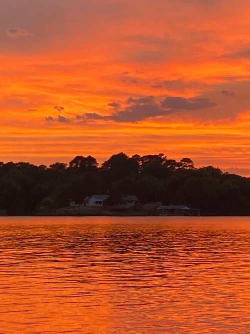 A vibrant sunset casts orange and pink hues over a calm lake, reflecting the colors on the water's surface.