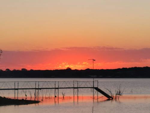 A serene sunset over a lake, with vibrant orange and pink hues reflecting on the water and a silhouette of a dock.