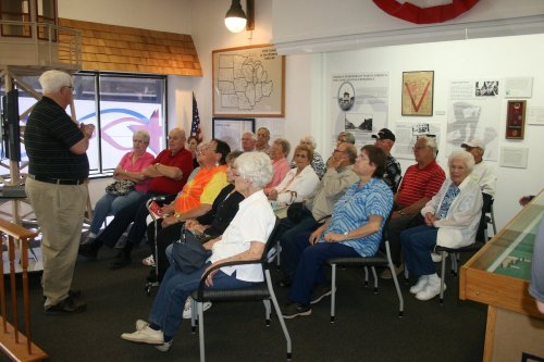A group of seniors attentively listening to a speaker in a museum setting.