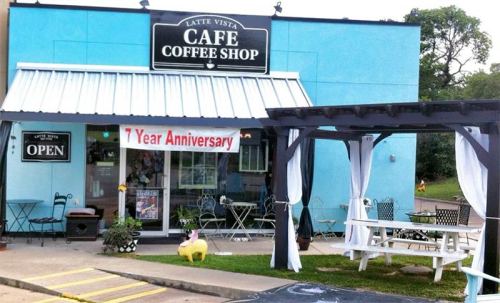A blue coffee shop with a sign reading "Latte Vista Café," featuring outdoor seating and a banner for its 1-year anniversary.