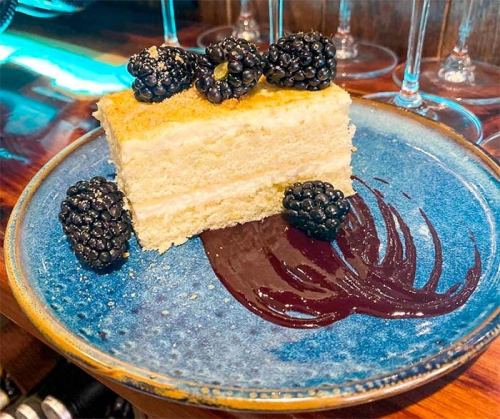 A slice of cake topped with blackberries, served on a blue plate with a drizzle of chocolate sauce.