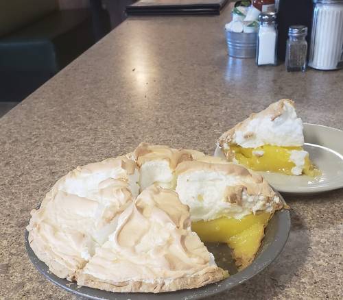 A lemon meringue pie with several slices cut, sitting on a countertop next to a single slice on a plate.
