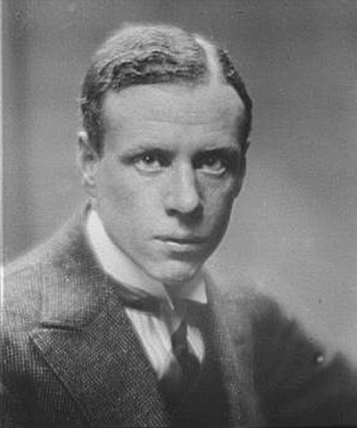 Black and white portrait of a young man in a suit, looking directly at the camera with a serious expression.