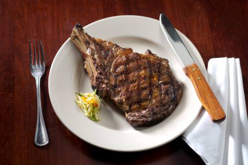A grilled ribeye steak on a white plate, accompanied by a small serving of coleslaw and a knife and fork.