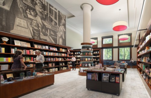 A modern bookstore with wooden shelves, a large mural, and customers browsing books in a bright, inviting space.