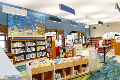 A bright library interior with colorful bookshelves, a mural, and modern lighting fixtures.