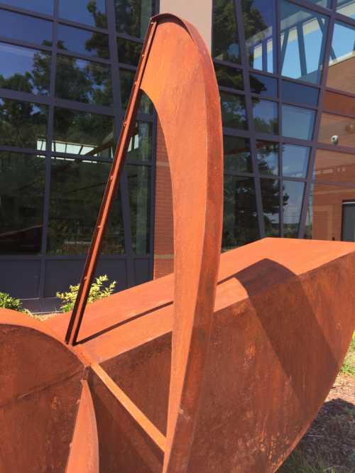 A large, rusted metal sculpture with curved shapes, set against a modern glass building.