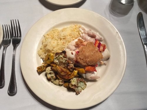 A plate of food featuring rice, seafood, and roasted vegetables, served on a white dish with utensils nearby.