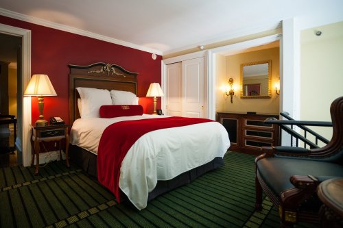 Cozy hotel room featuring a red accent wall, a queen bed with a red throw, and elegant furnishings.