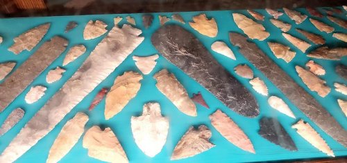 A collection of various stone tools and arrowheads displayed on a blue surface.