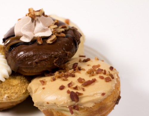 A close-up of assorted donuts topped with chocolate, caramel, and nuts on a white plate.
