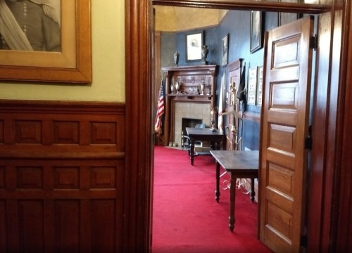 View of a room with red carpet, wooden furniture, and framed artwork, seen through an open door.