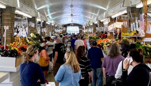 A bustling market filled with people shopping for fresh produce, with colorful fruits and vegetables on display.