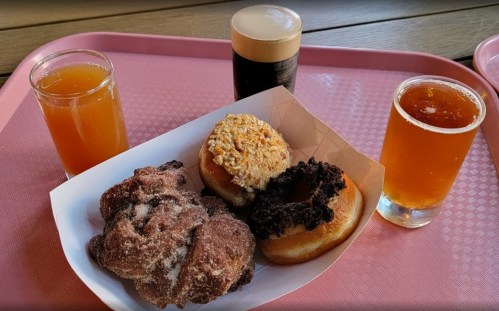A tray with two glasses of beer, two donuts topped with nuts and chocolate, and a sugar-coated pastry.