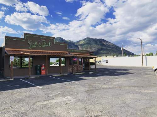 A restaurant with a sign reading "Let's Eat," set against a backdrop of mountains and a partly cloudy sky.