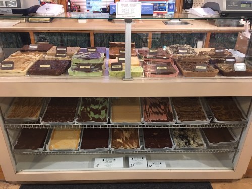A display case filled with various types of fudge, labeled and arranged in neat rows.