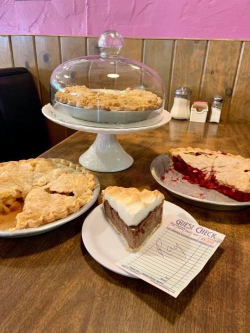 A table with four delicious pies: apple, cherry, chocolate cream, and a guest check on a plate.