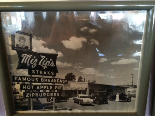 Black and white photo of a vintage diner sign and cars, featuring "Miz Zip's Steaks" and "Famous Breakfast."