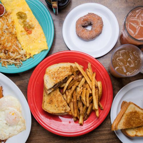 A colorful spread of breakfast items: an omelet, hash browns, a donut, fries, and drinks on a wooden table.