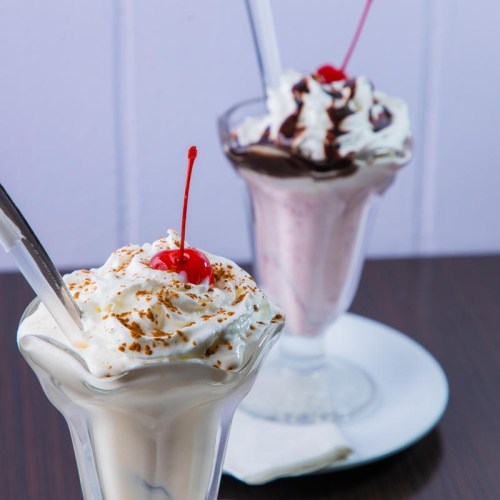 Two delicious ice cream sundaes topped with whipped cream and cherries, served in clear glass dishes.