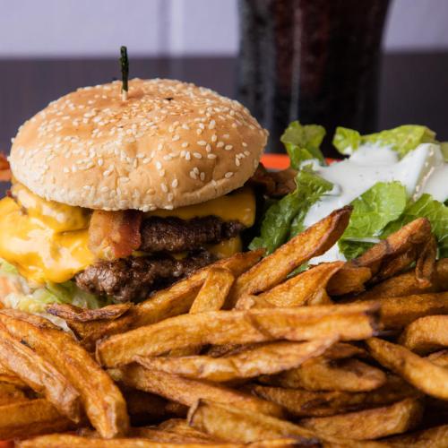 A juicy cheeseburger with bacon, lettuce, and a sesame seed bun, served with crispy fries and a side of salad.