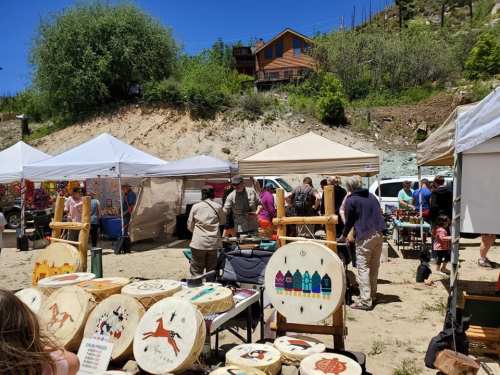 A vibrant outdoor market with tents, people browsing, and colorful wooden crafts displayed on tables.