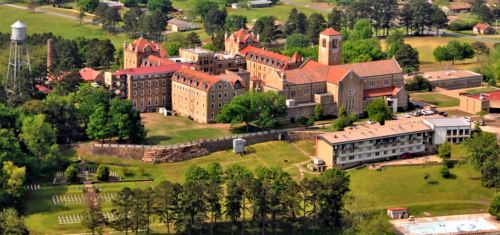 Aerial view of a large historic building complex surrounded by greenery and a water tower in the background.