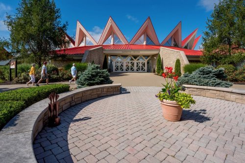 A modern building with a red roof and triangular peaks, surrounded by greenery and a paved walkway.