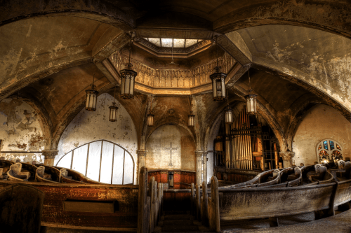 Interior of an abandoned church featuring ornate architecture, stained glass, and vintage wooden pews.
