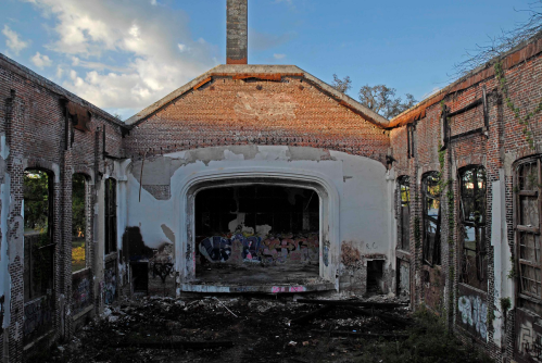 Abandoned building interior with crumbling walls, graffiti, and a large empty space where a stage once stood.