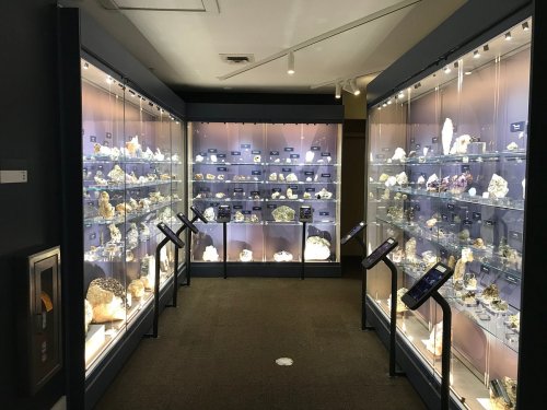 A well-lit display room showcasing various mineral specimens in glass cases, with informational plaques and a clean floor.