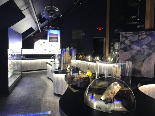 A dimly lit museum exhibit featuring display cases with various geological specimens and illuminated information panels.