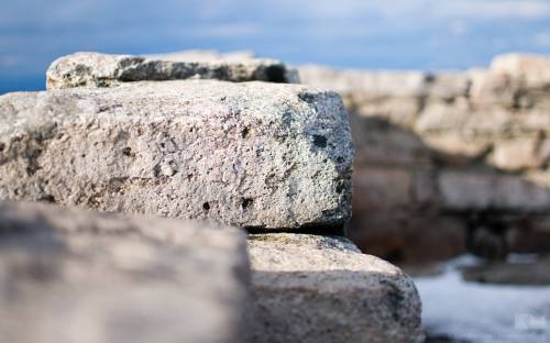 Close-up of weathered stone blocks with a blurred background of rocky terrain and a cloudy sky.