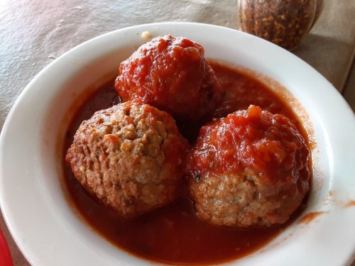 Three large meatballs covered in marinara sauce, served in a white bowl.