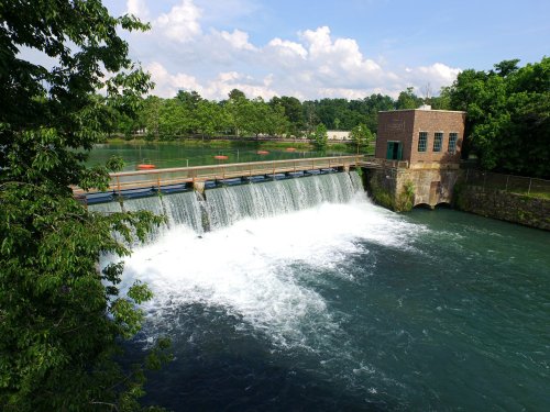 A scenic view of a dam with water cascading over it, surrounded by lush greenery and a clear blue sky.