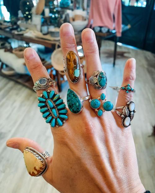 A hand displaying multiple silver rings with various gemstones, including turquoise and amber, in a stylish setting.