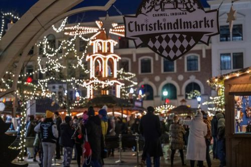 A festive market scene in Carmel, Indiana, with twinkling lights, a carousel, and crowds enjoying the holiday atmosphere.