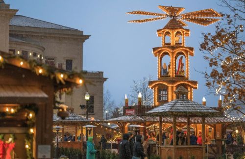 A festive market scene with a decorated wooden structure and people enjoying the holiday atmosphere in the evening.