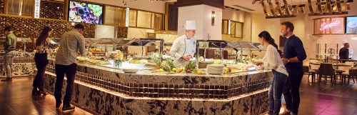 A buffet restaurant scene with a chef serving food, guests selecting dishes, and a vibrant dining atmosphere.