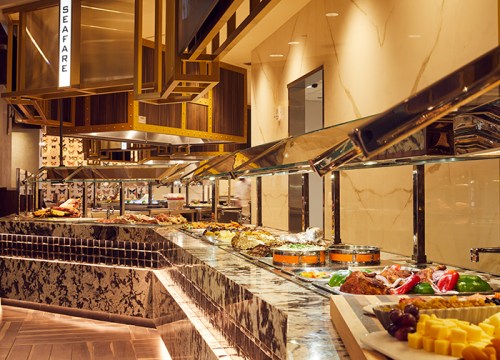 A buffet with a variety of dishes, including seafood, meats, and cheeses, in a modern dining setting.