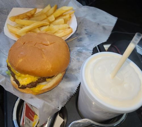 A cheeseburger with lettuce, fries, and a milkshake in a car cup holder.