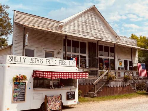 A rustic building with a food truck in front, offering fried pies, and decorated with an American flag.