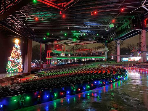 A festive outdoor venue decorated with colorful lights and a large Christmas tree, reflecting a holiday atmosphere.