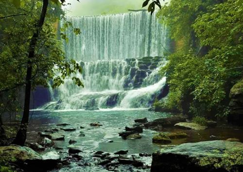 A serene waterfall cascades over rocks, surrounded by lush green trees and misty air.